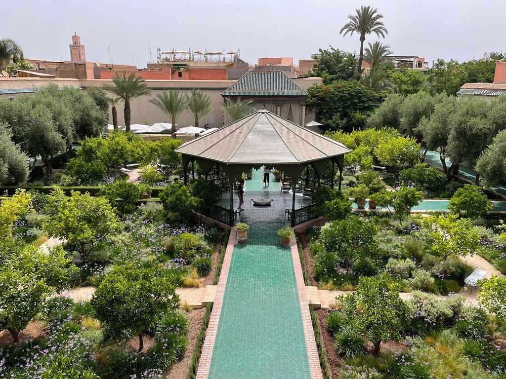 Fonte central rodeada por azulejos no Le Jardin Secret com vegetação exuberante ao redor