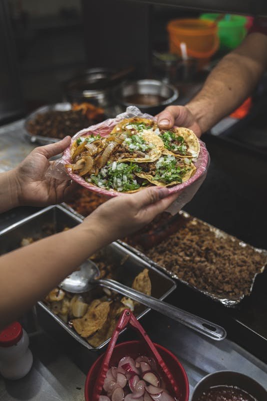 Close-up of authentic Mexican tacos being served at a street food stall, rich in colors and flavors.