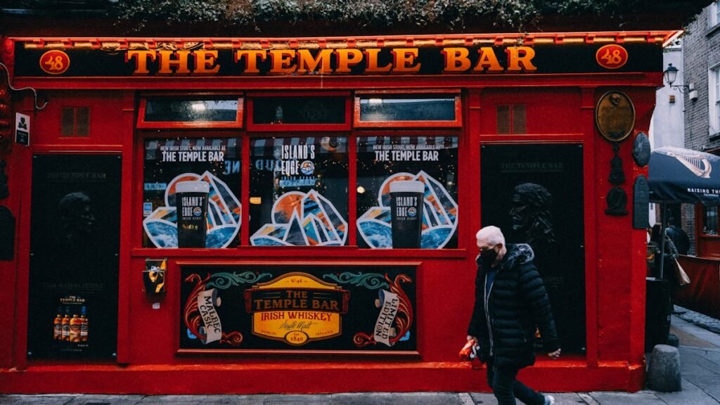 a man walking past a red building with a sign on it in front of Temple Bar - Dublin