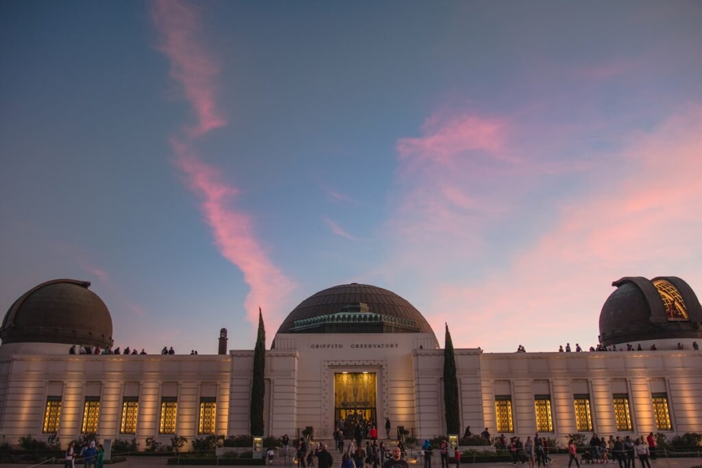Griffith Observatory no alto das colinas com o letreiro de Hollywood ao fundo e o pôr do sol colorido