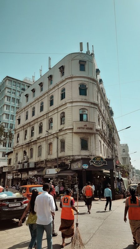 a group of people walking down a street next to a tall building in colaba causeway market